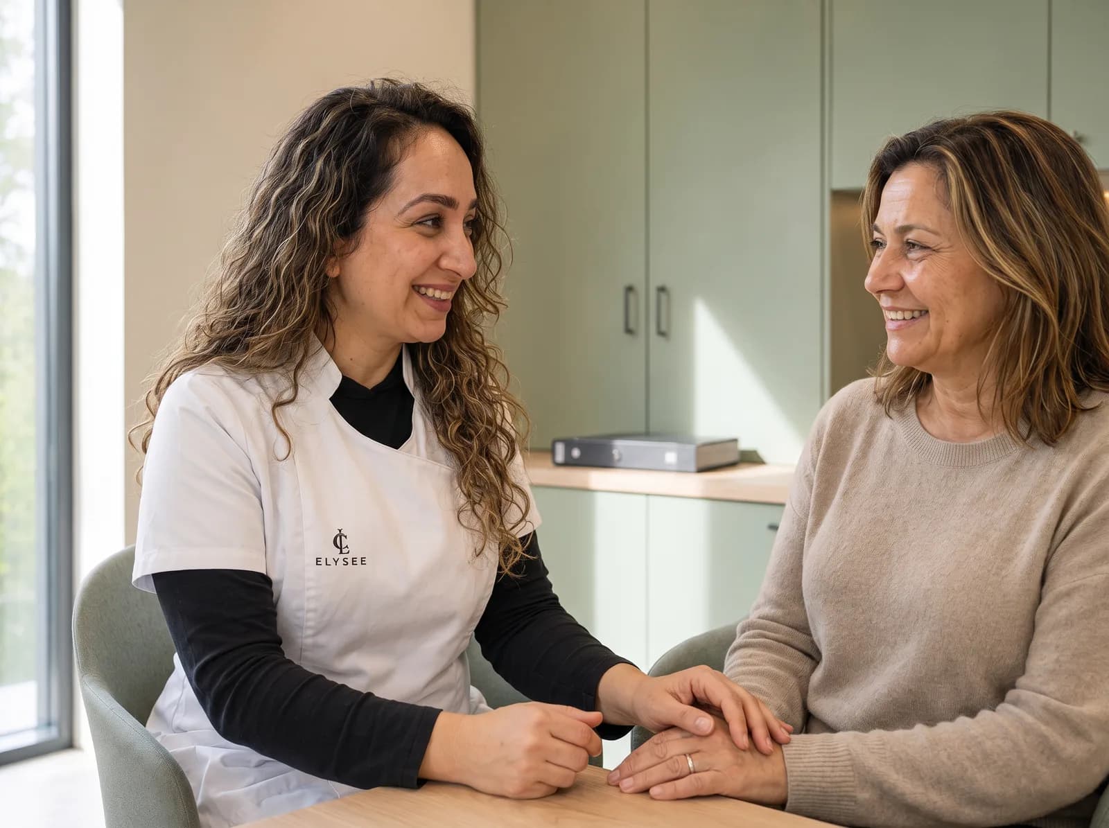 Drs. Donija Azim en een cliënte zitten naar elkaar toegebogen in gesprek in de kliniek